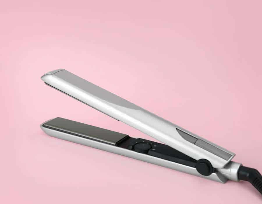 a silver hair straightener on a pink background